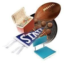 A tailgate party setup including a football, a grill with food, a blue state pennant, a cooler, and a portable seat.