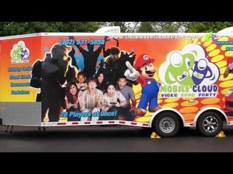 Side view of a vibrant orange trailer for a mobile video game party featuring Mario and a group of excited gamers.