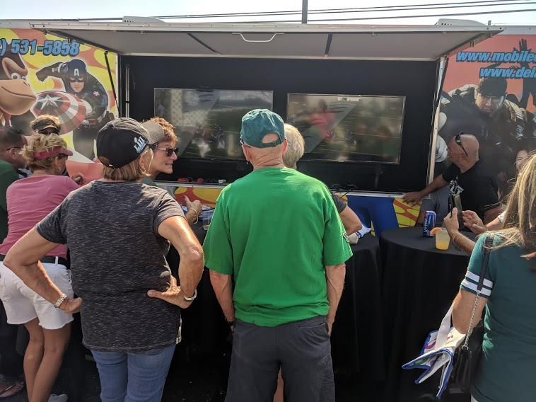 A group of people watch two large video screens mounted in an outdoor mobile gaming trailer.