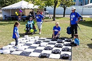 A group of people playing a game with large black and white checkers on an outdoor mat under a sunny sky.