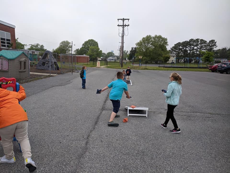 Children playing a cornhole game on an outdoor paved playground.