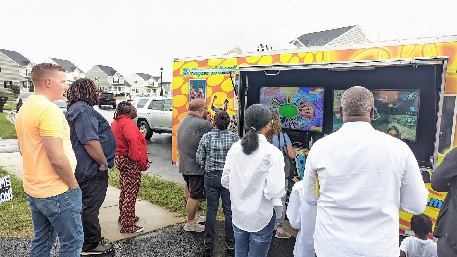 A group of people standing outside and watching games on screens displayed inside a mobile video game truck.