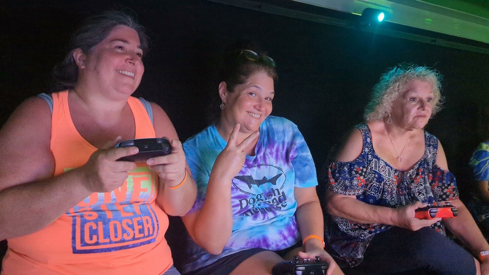 Three people sitting in a dark room, holding game controllers and smiling.