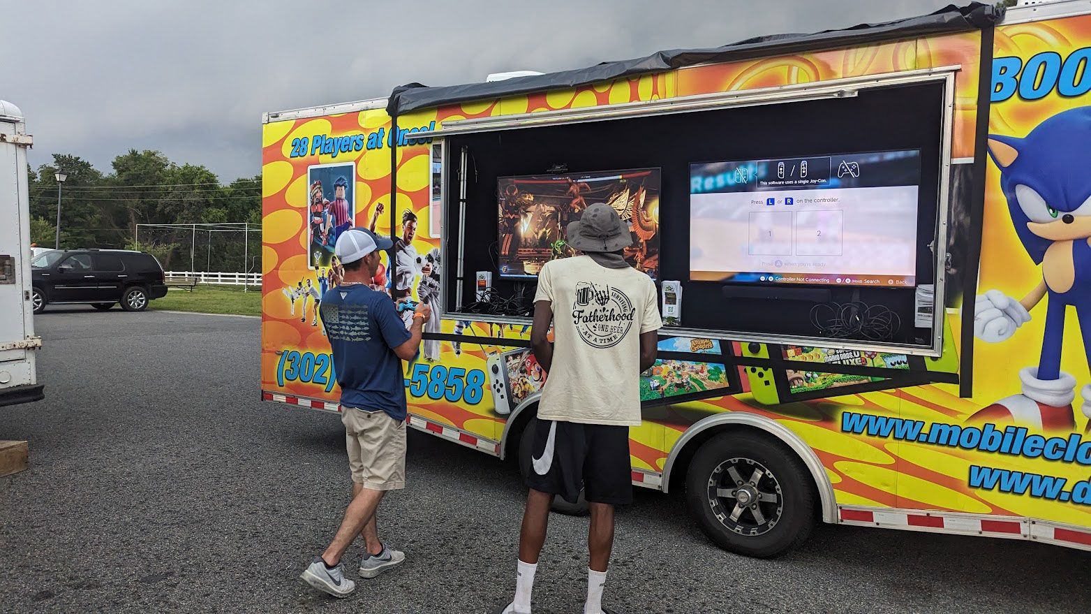 Two people stand outside a brightly colored Sonic the Hedgehog mobile gaming truck, playing video games.