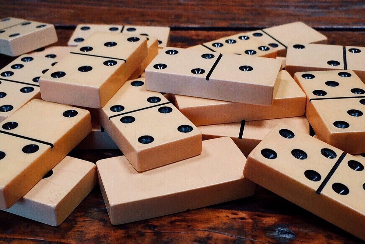 A pile of light-colored wooden dominoes with black pips scattered on a dark wooden surface.