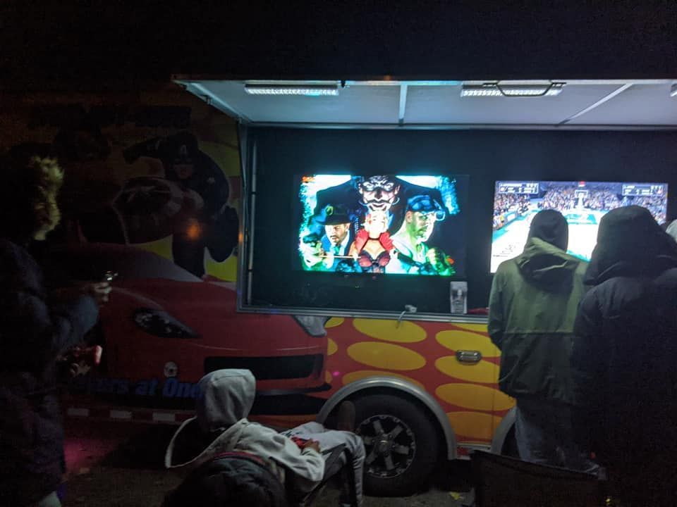 A mobile video game trailer at night shows people playing games on large mounted screens.