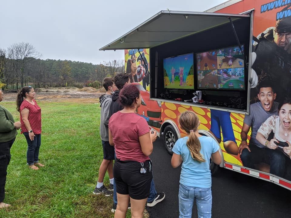 People stand outside a mobile video game trailer watching gameplay on two large external screens.