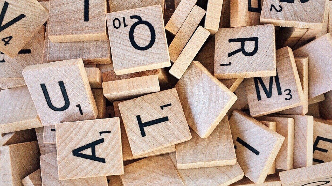 A pile of wooden Scrabble letter tiles showing various letters, including Q, U, A, T, R, and M.