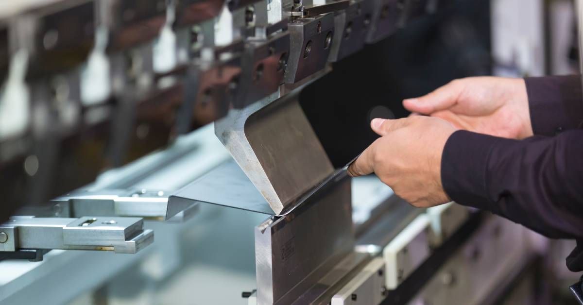 A person wearing a black shirt uses a machine to bend a piece of sheet metal on a manufacturing floo