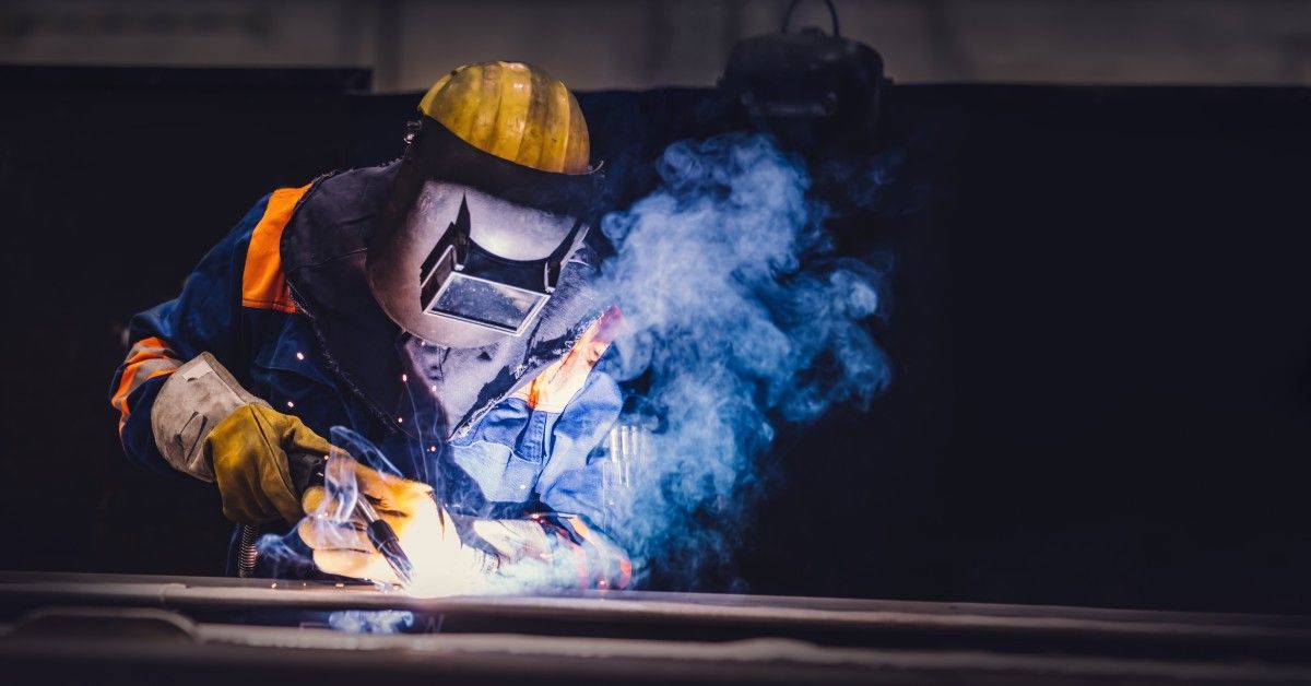 A worker wearing a protective mask and insulated clothing while using a welder.