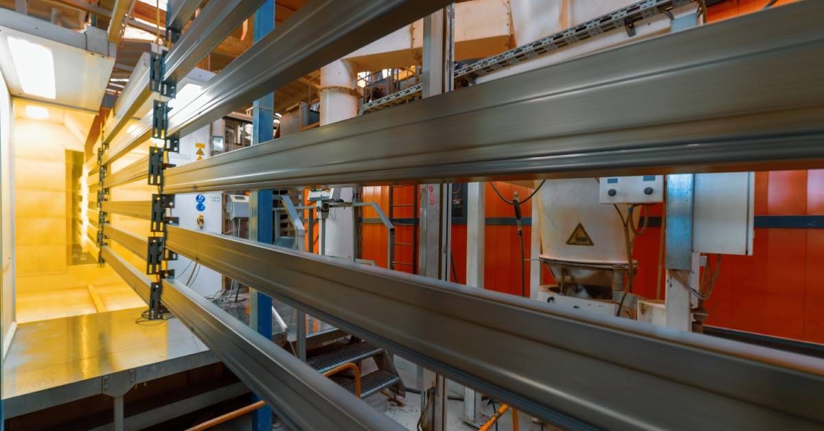 Rows of metal beams in a machine on a factory floor receiving industrial coating for corrosion.