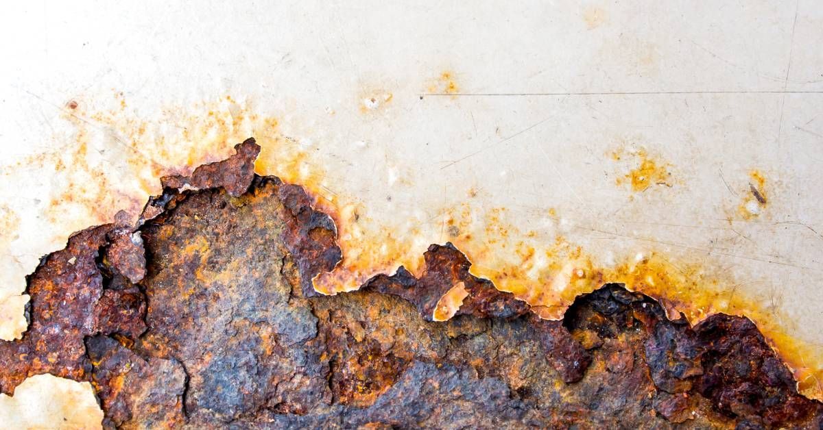 A close-up of metal surface corrosion. It’s covered in red and yellow rust with flakes chipping off.