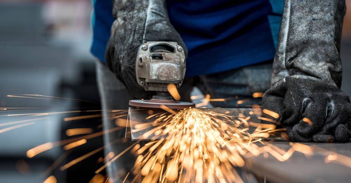 A worker wears protective gloves to use a tool and cut into metal. Sparks are coming off of it.