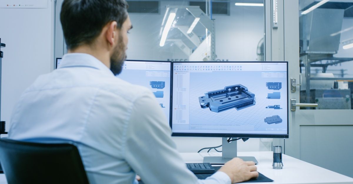 A man in a white shirt sitting in front of a computer. He is using a CAD program to design a new component.