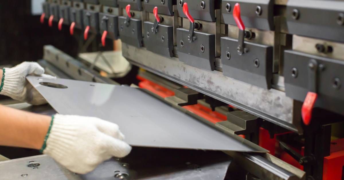 A person’s gloved hands holding sheet metal with a hole punched into it in front of a machine.