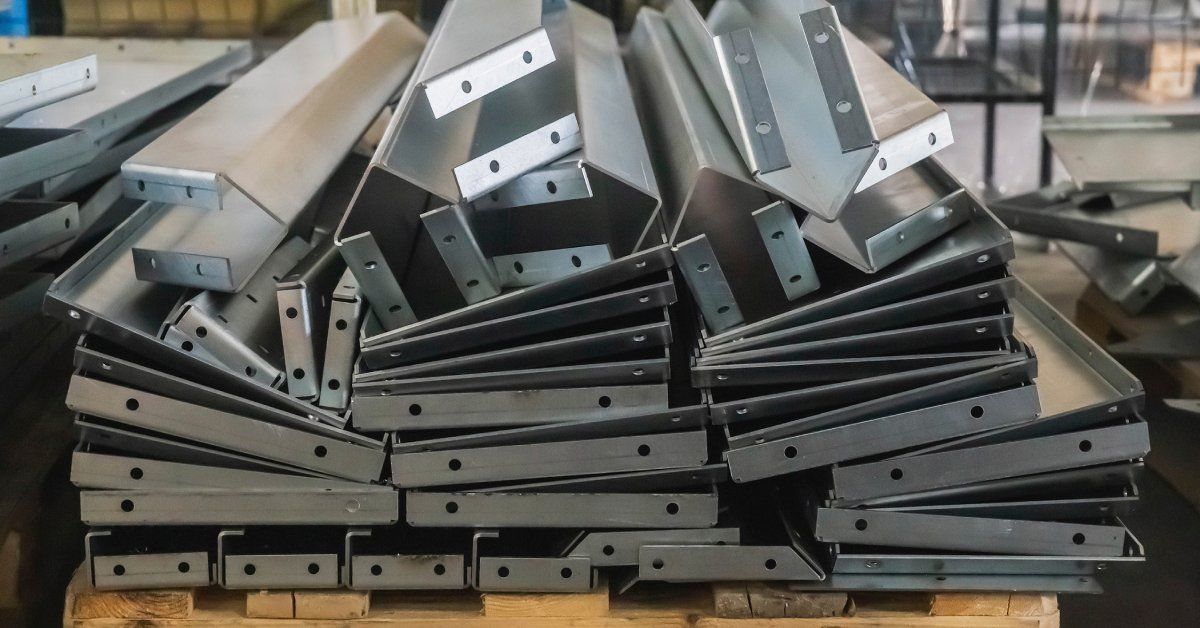 A pile of manufactured metal products with small holes punched in them lying on a wooden pallet in a factory.