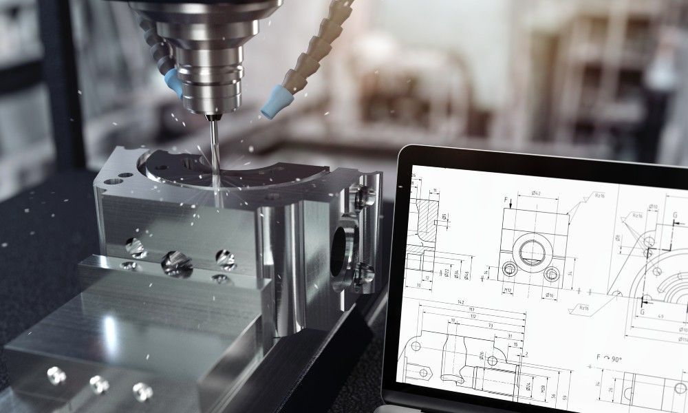 A CNC machine next to an open laptop. The machine is following a digital design to develop a metal