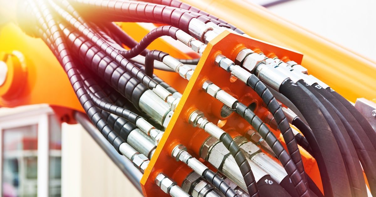 A close-up of several black hoses part of a hydraulic system in a large piece of yellow equipment.