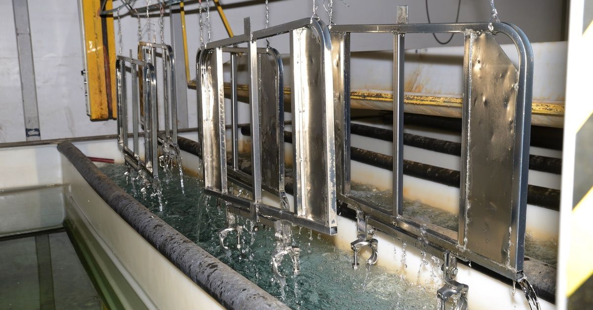 Multiple large metal pieces are suspended out of a tank filled with liquid to electroplate them. The pieces are dripping into the tank.