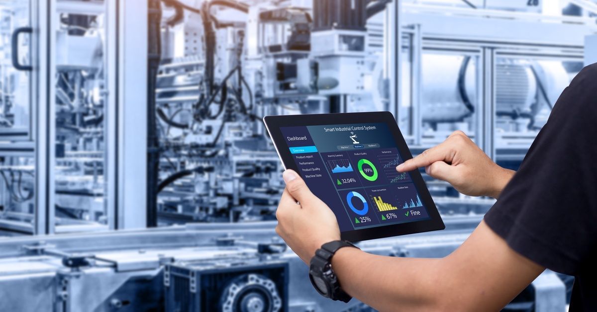 A person holds a tablet with performance metrics while standing in front of industrial equipment.