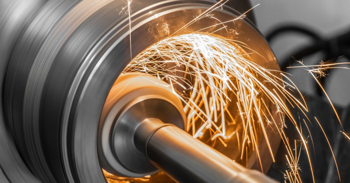 A spinning grinding wheel inside a spinning cylindrical metal piece creates bright sparks.