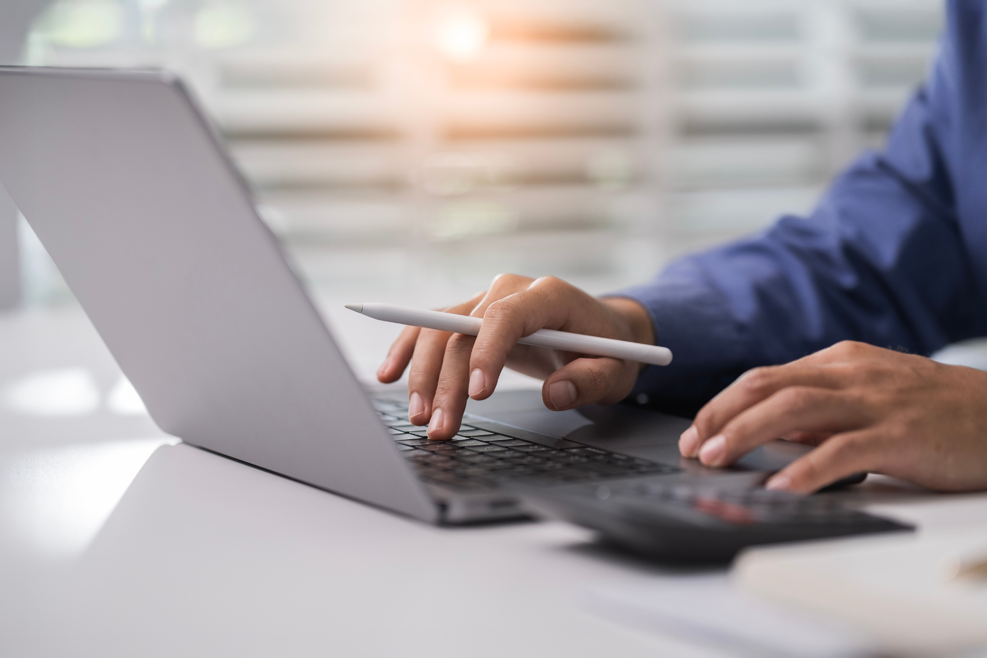 Hands typing on a laptop beside a calculator on a desk.