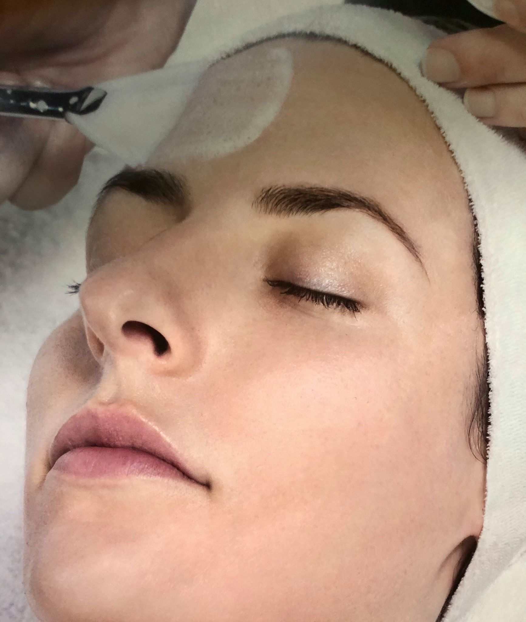 A woman is getting a facial treatment with her eyes closed.