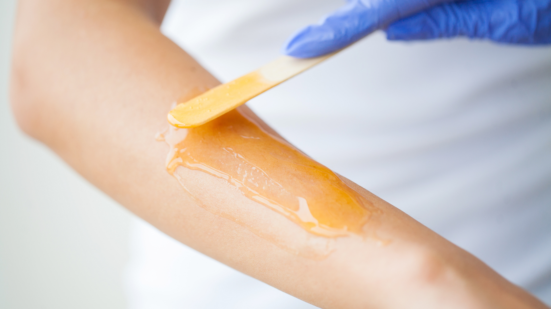 A woman is getting her arm waxed with a spatula.