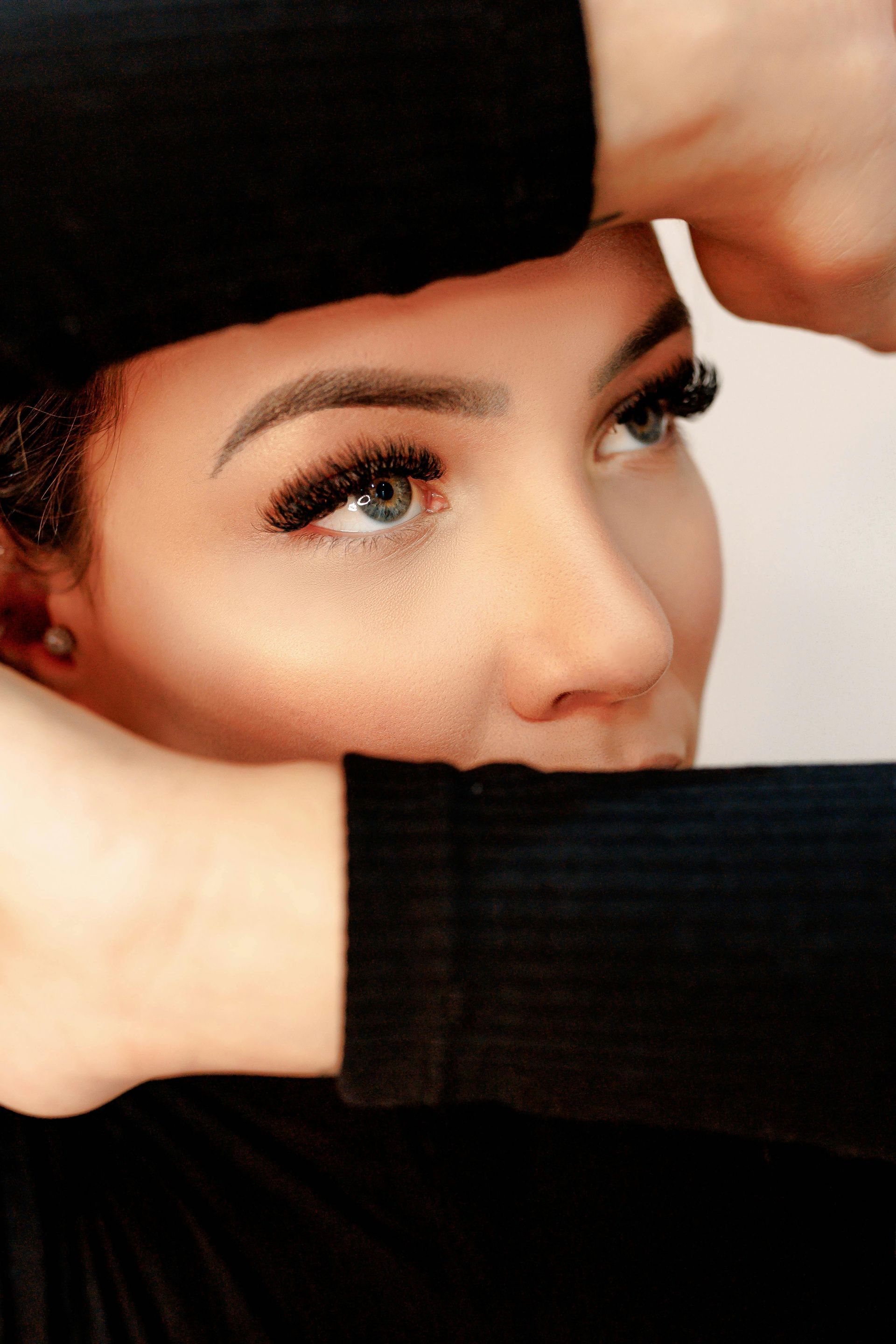 A woman with long eyelashes is covering her face with her hands.