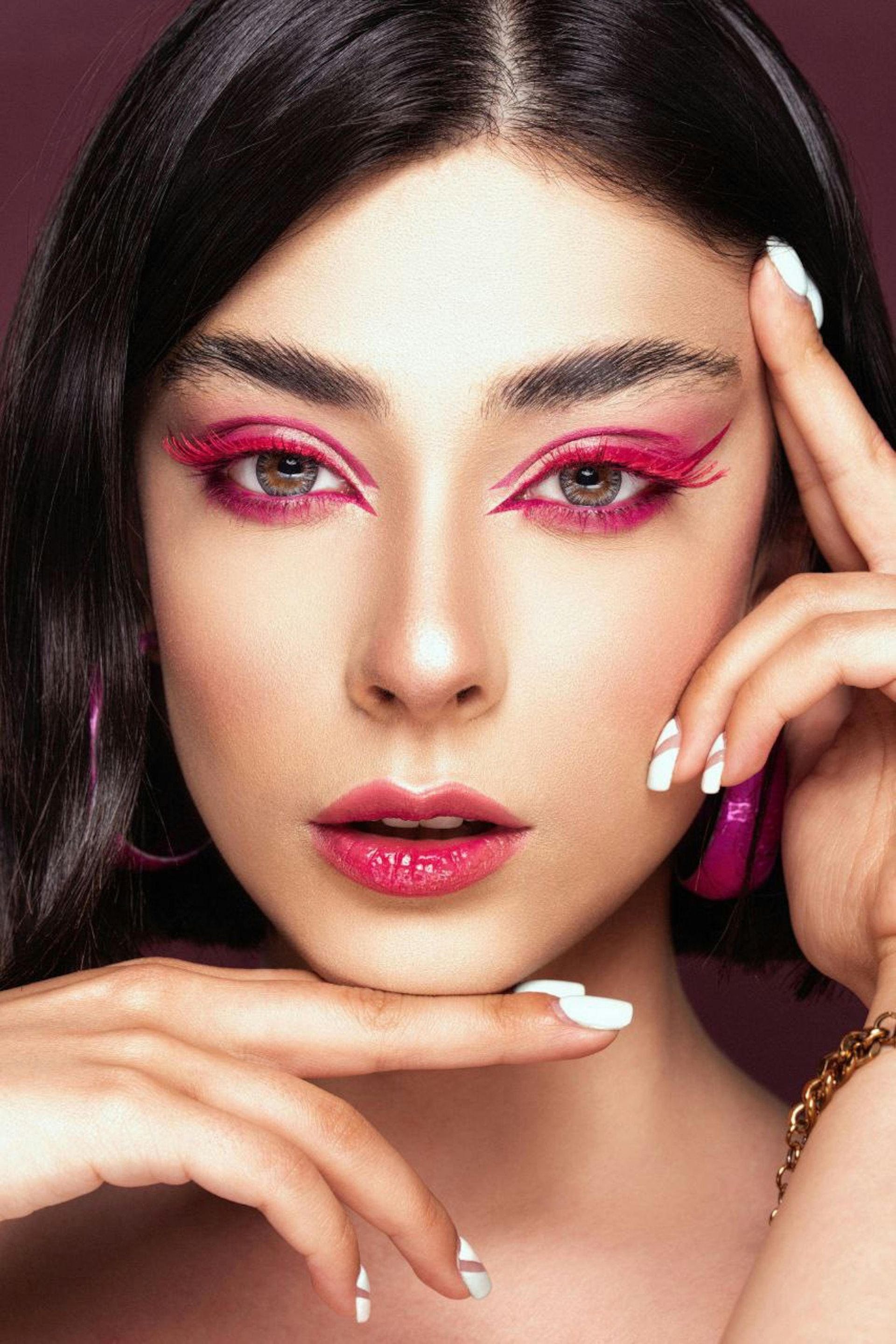 A close up of a woman 's face with pink eye shadow and earrings.
