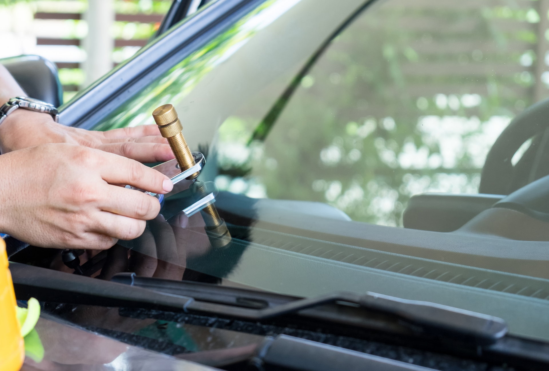Person repairing a windshield crack with a repair tool.