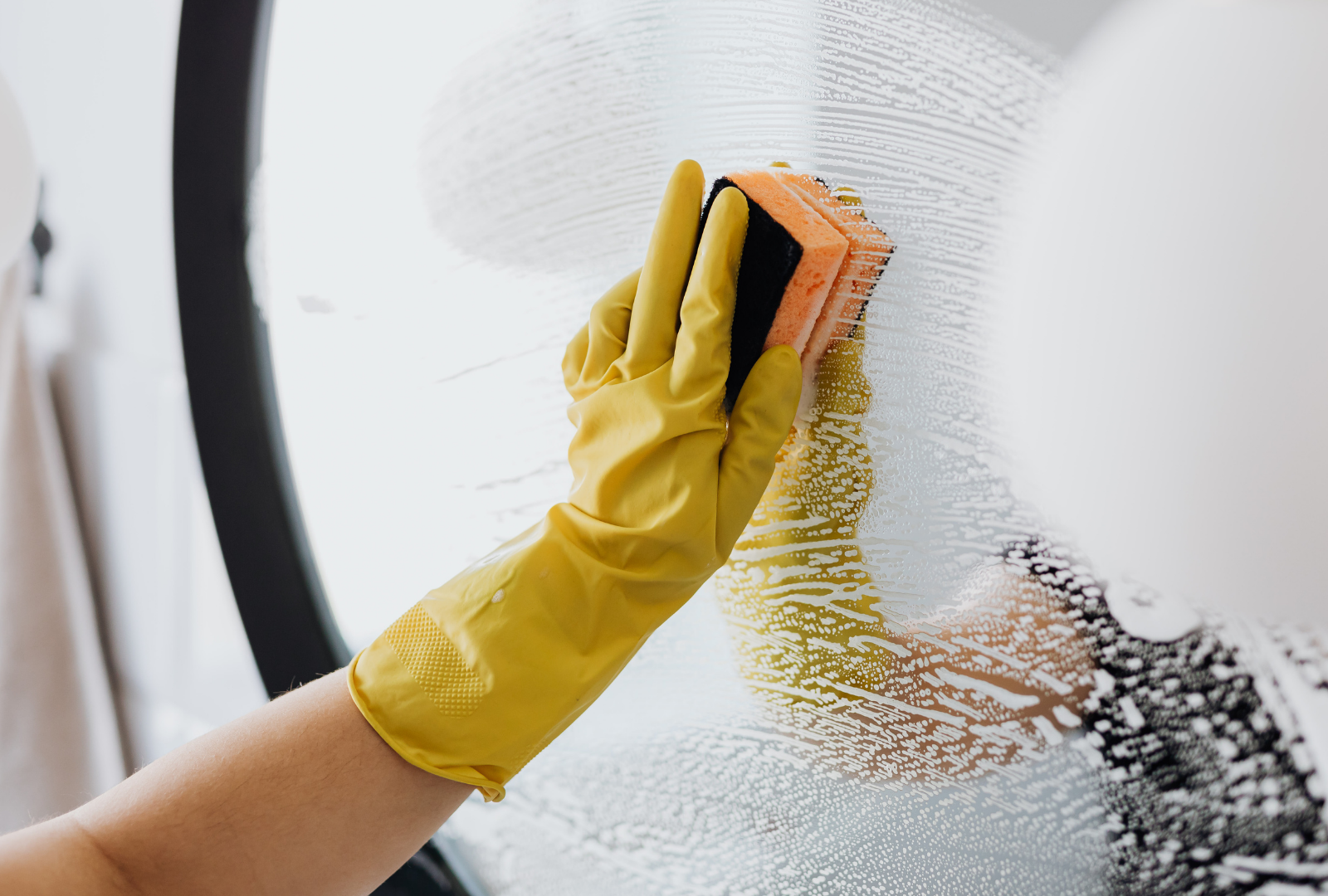 Person in yellow gloves cleaning a window with a sponge.