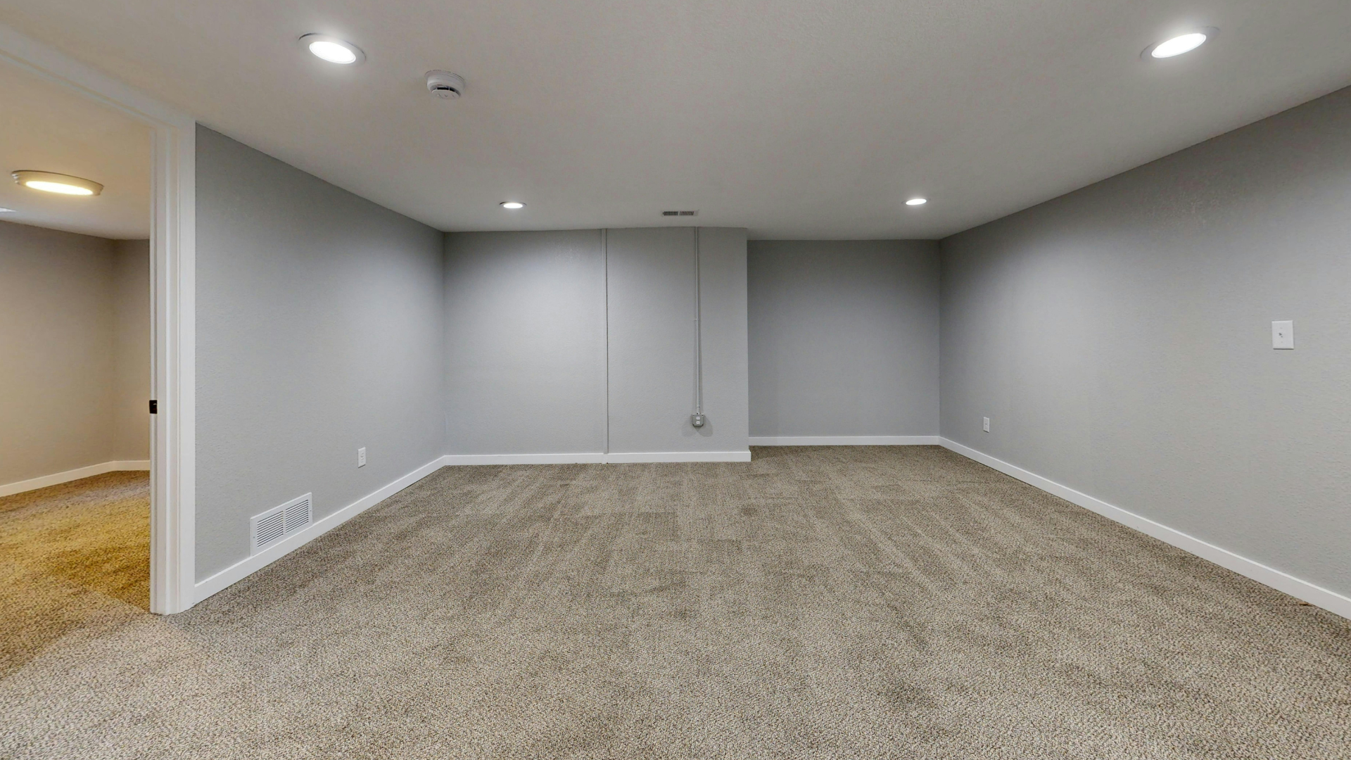 Empty room with gray walls, beige carpet, recessed lights. Doorway leads to another room.