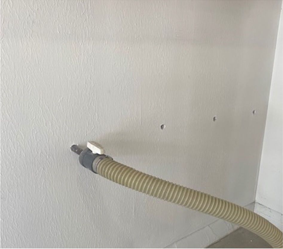 A vacuum hose is attached to a white wall.