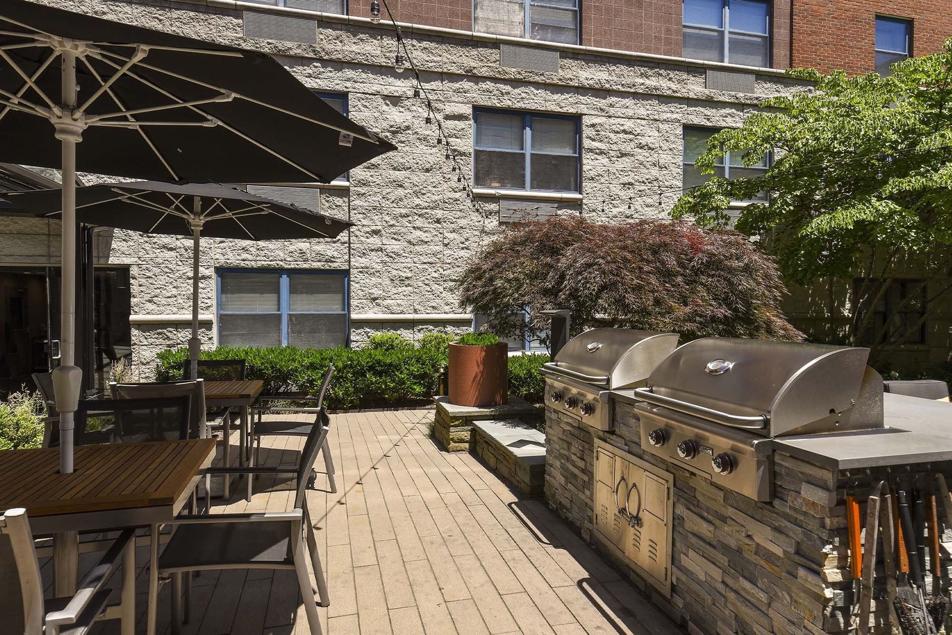 Patio with brick flooring, tables, chairs, and outdoor kitchen with a grill under umbrellas.