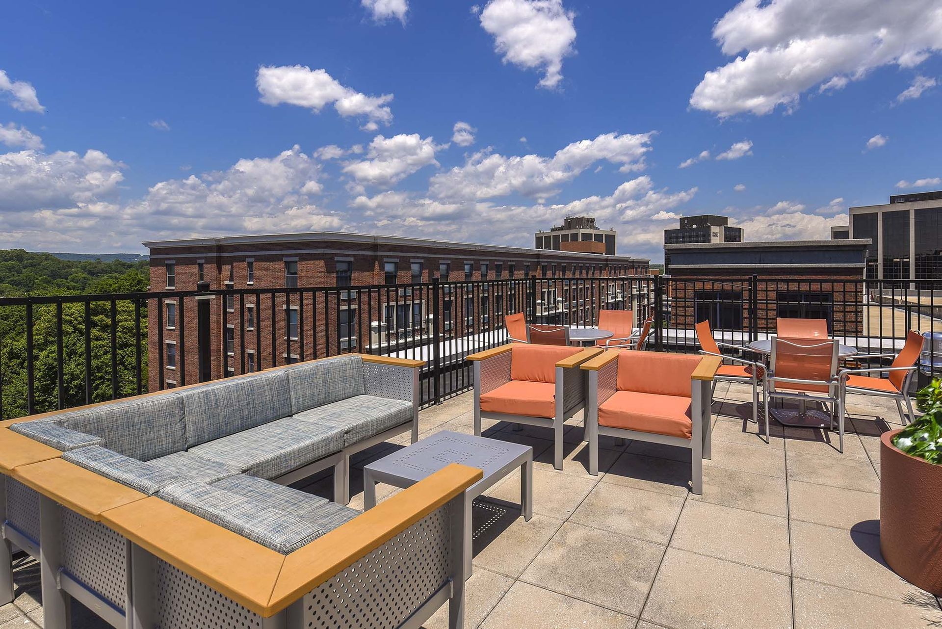 Rooftop patio with gray sectional, orange chairs, and a small table on a sunny day.