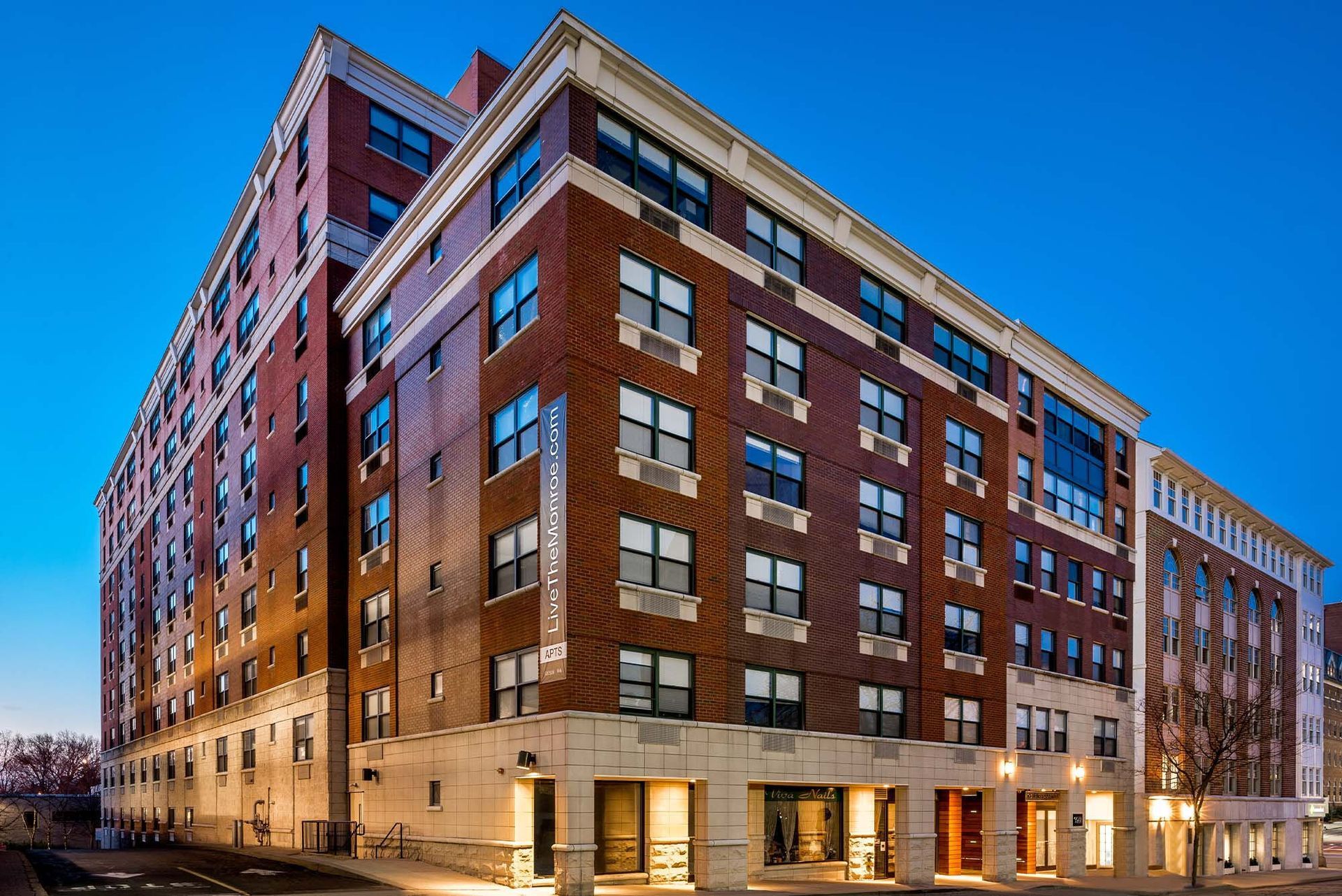Multi-story brick building with cream-colored accents, windows, and entrance doors under a blue sky.