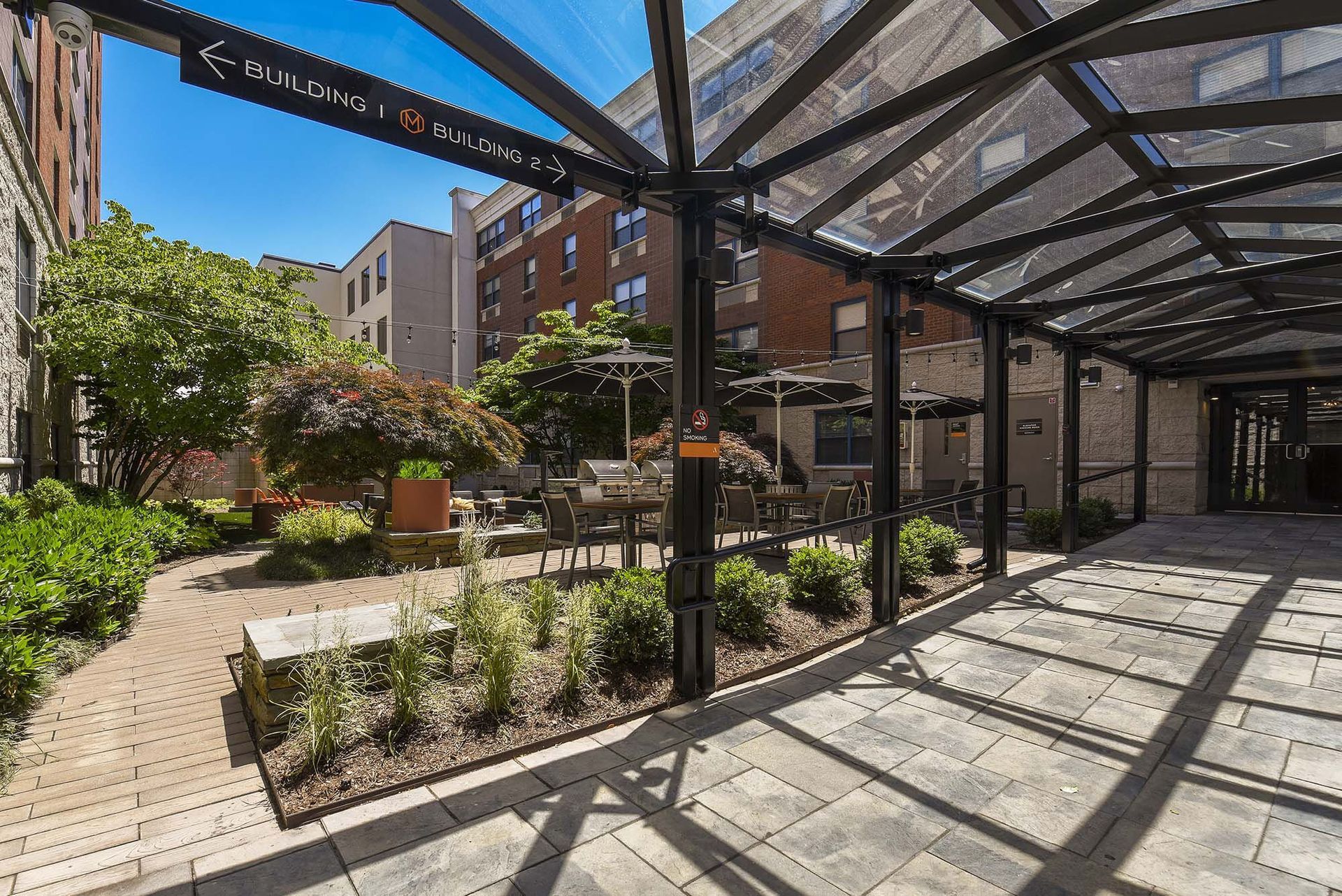 Covered walkway leading to outdoor patio with tables and trees.