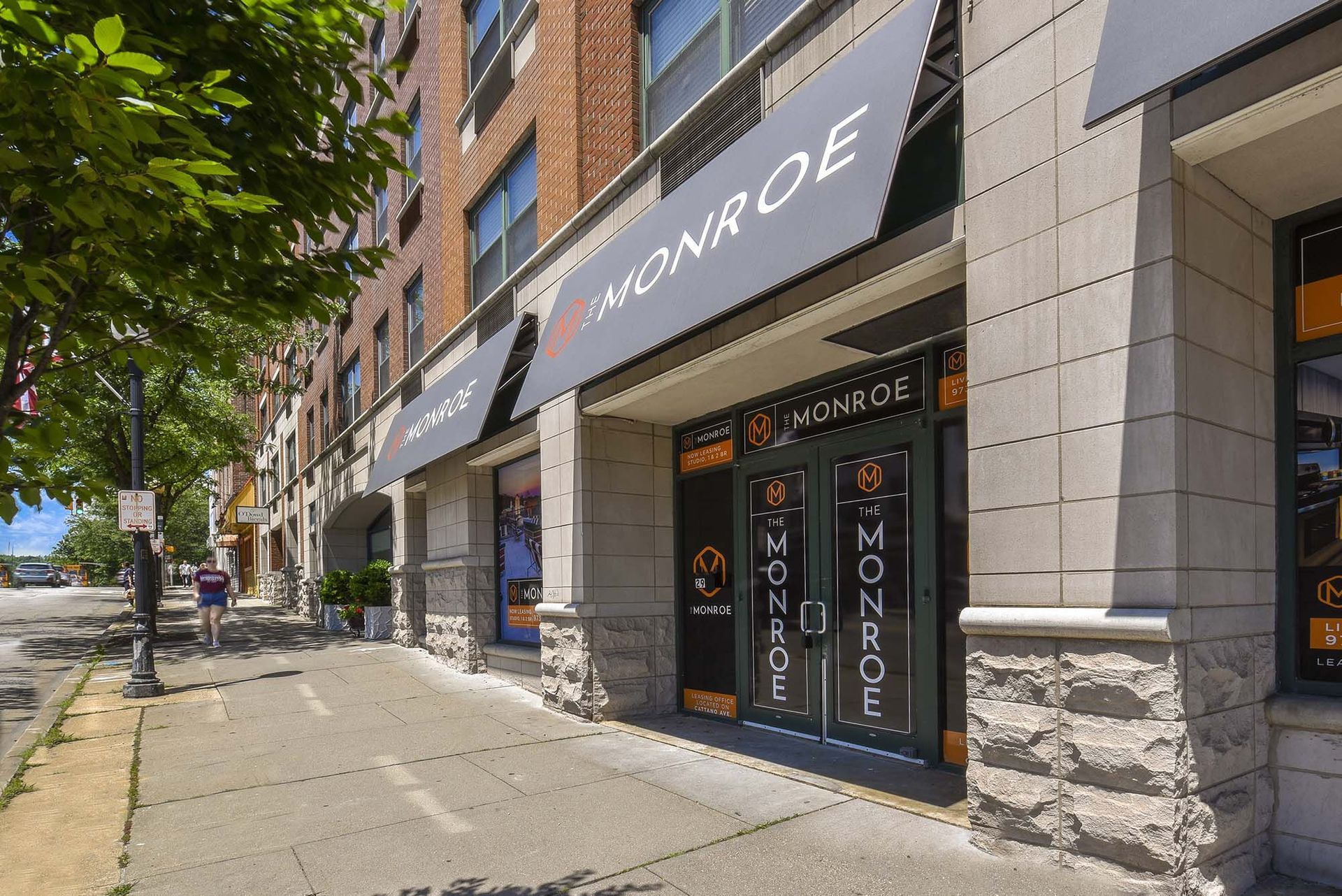 Monroe building storefront with black awnings, brick facade, and glass doors. A person walks on the sidewalk.