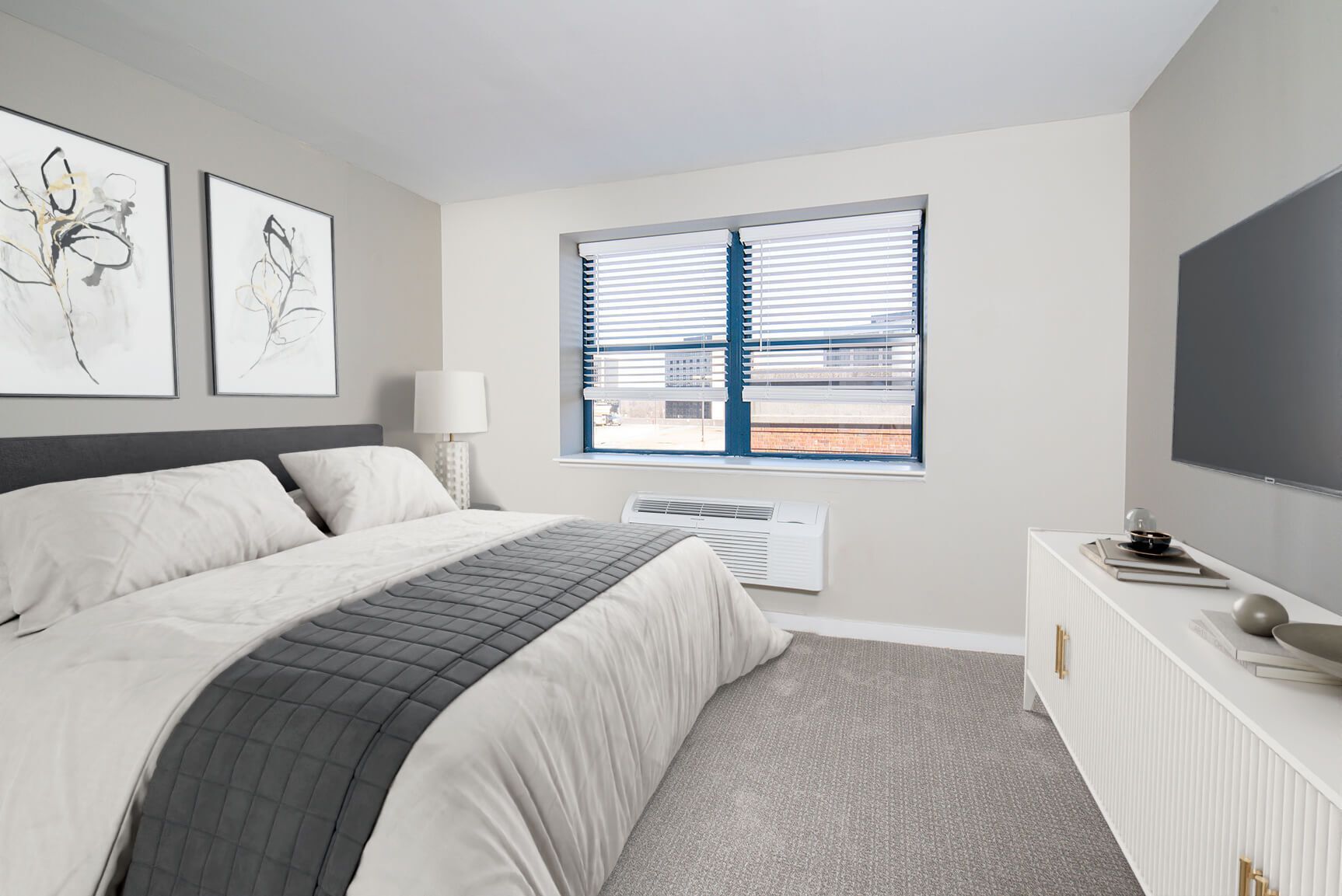 Bedroom with a bed, TV, window, and artwork. Gray and white color scheme.
