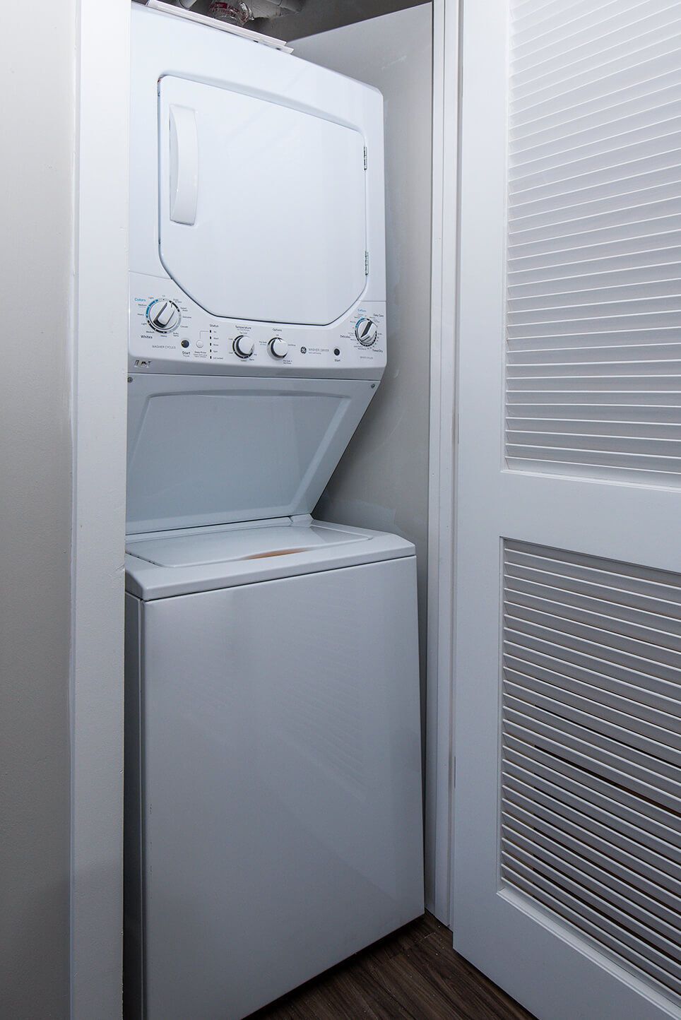 Stacked white washing machine and dryer in a closet, with a louvered door.