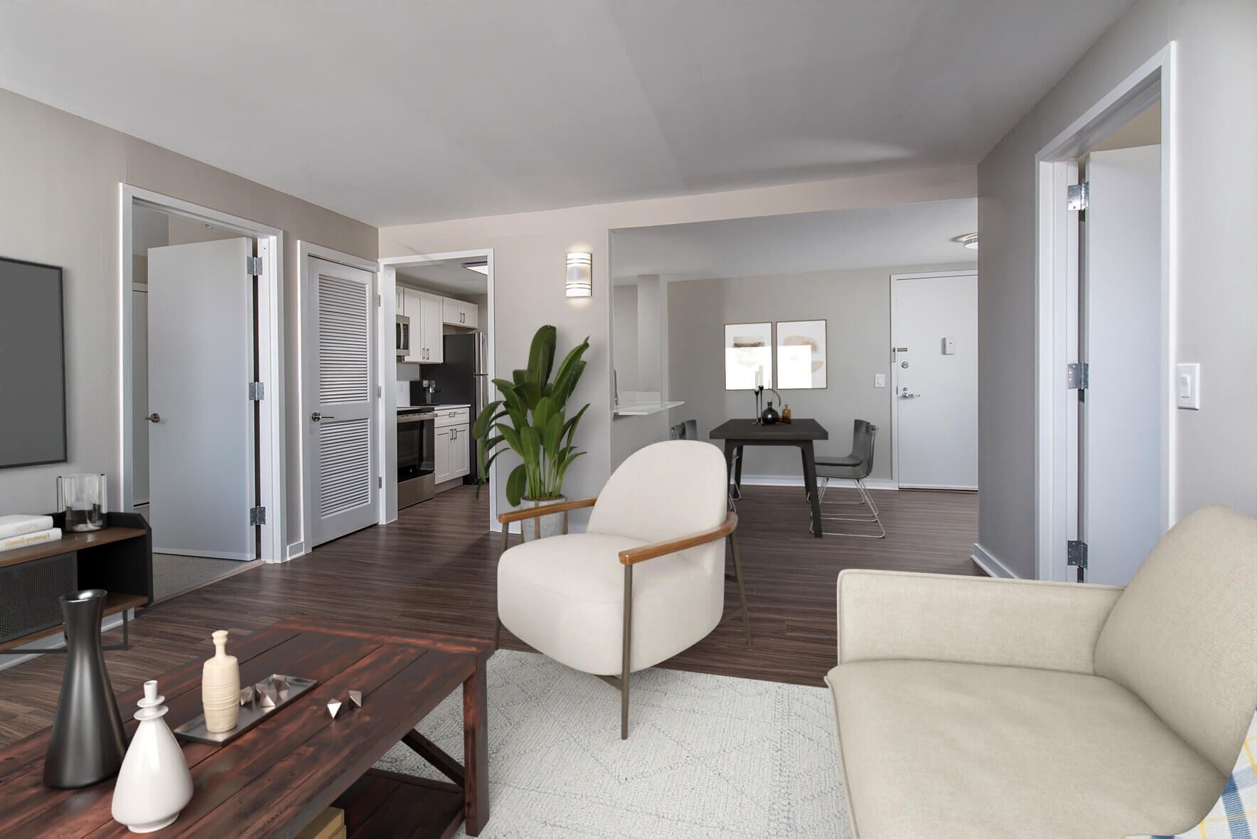 Spacious living room with white armchair, beige couch, dark wood floor, and open doorway to kitchen.