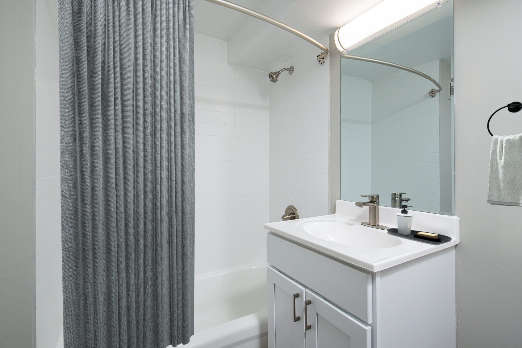 White bathroom with shower, vanity, and mirror; gray shower curtain and towel.