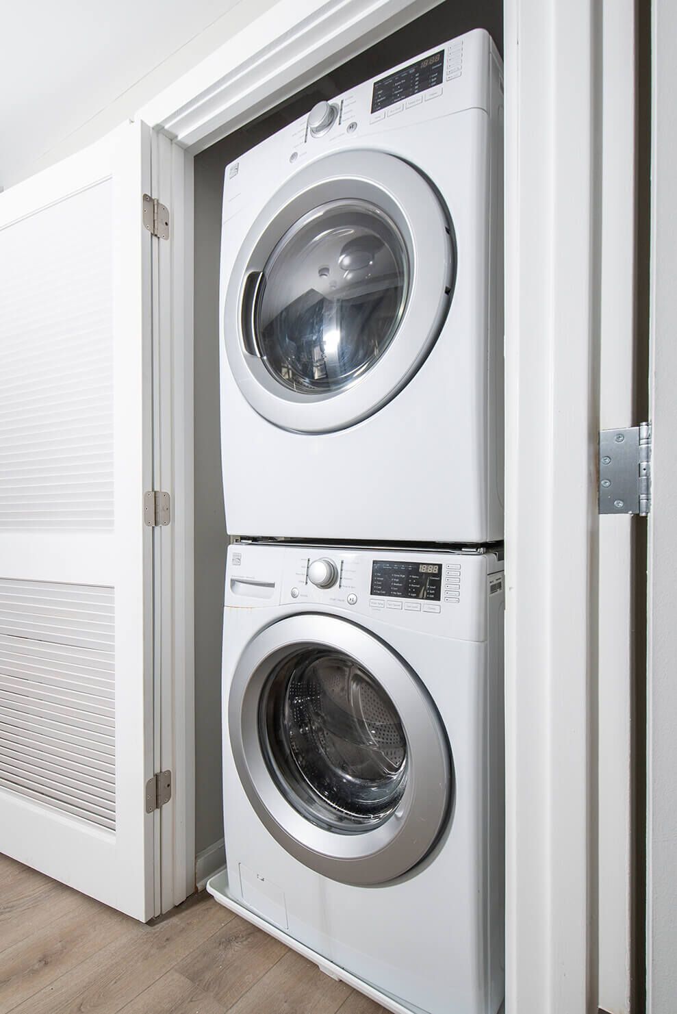 Stacked white washer and dryer units inside a closet with doors open.
