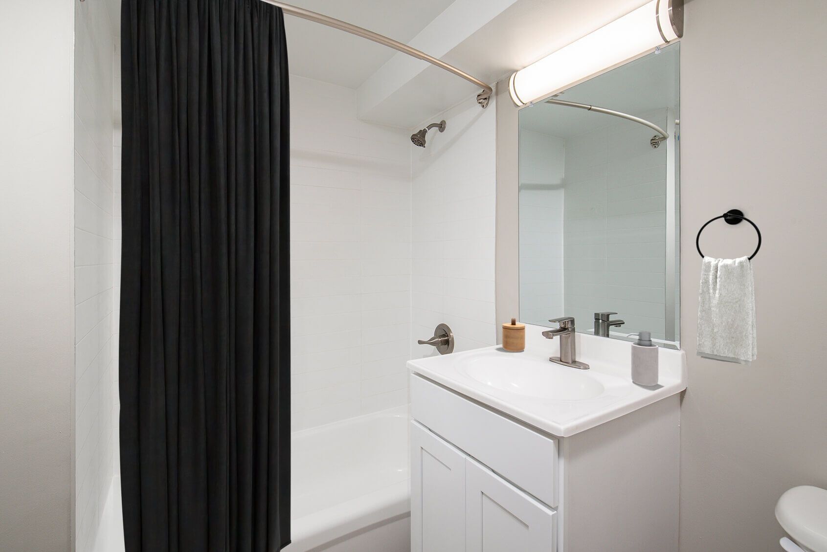 Bathroom with white walls and a white vanity. Black shower curtain and a towel ring.