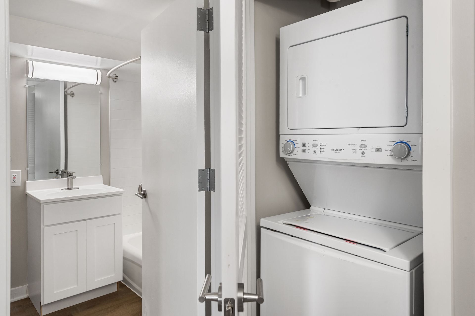 A small white bathroom with a stacked washer and dryer unit, a sink and vanity, and a shower with a shower curtain.