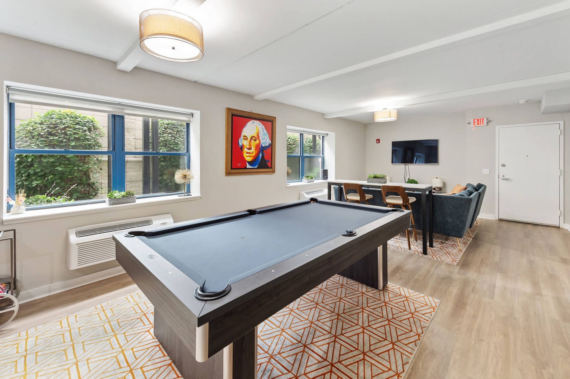 Pool table in a lounge with a painting, windows, seating, and a TV.