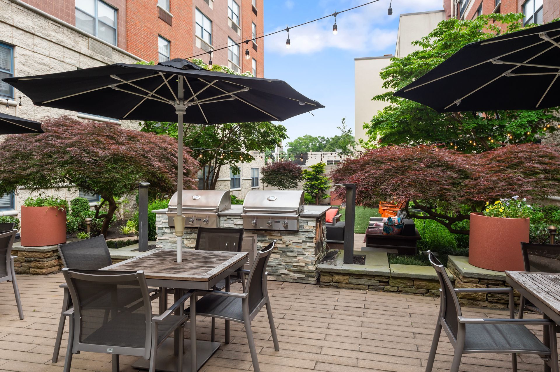 Outdoor patio with grills, tables, umbrellas, and trees.