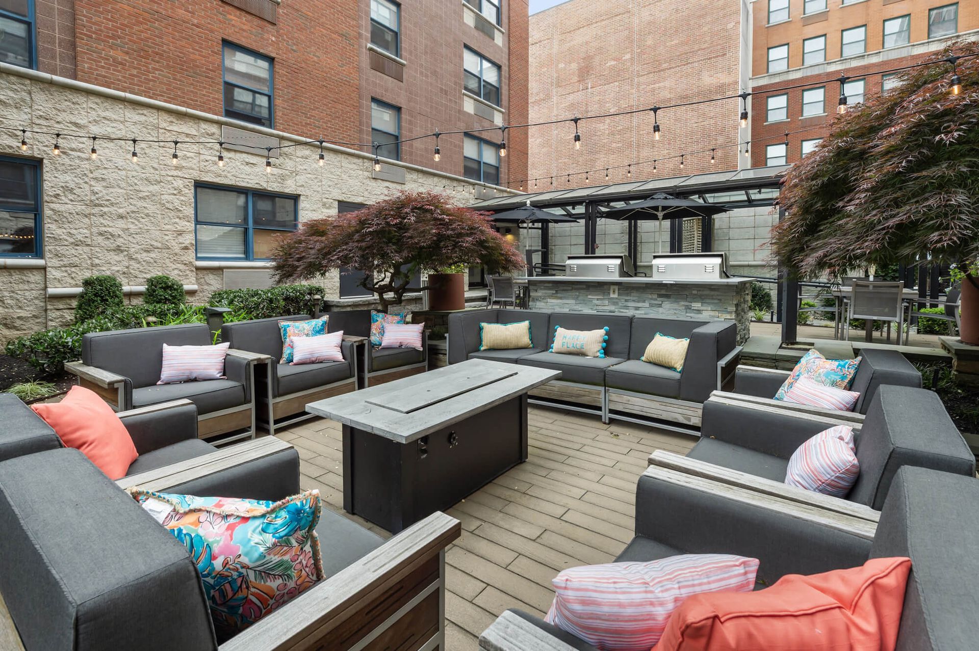 Outdoor seating area with couches, fire pit, and grill in a courtyard setting.