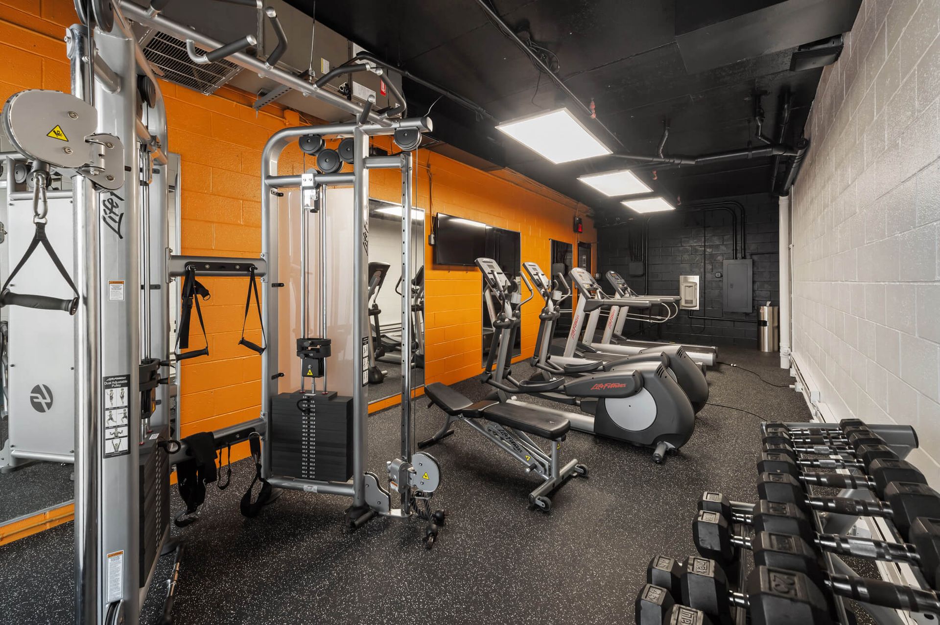 Gym with exercise machines, weights, and orange/black accents.
